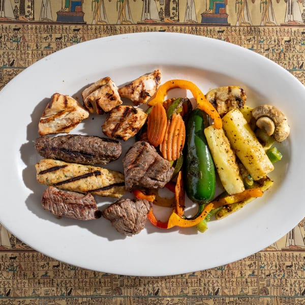 King Tut's grilled meat platter with chicken, kofta, beef, and colorful vegetables on an Egyptian-themed tablecloth.