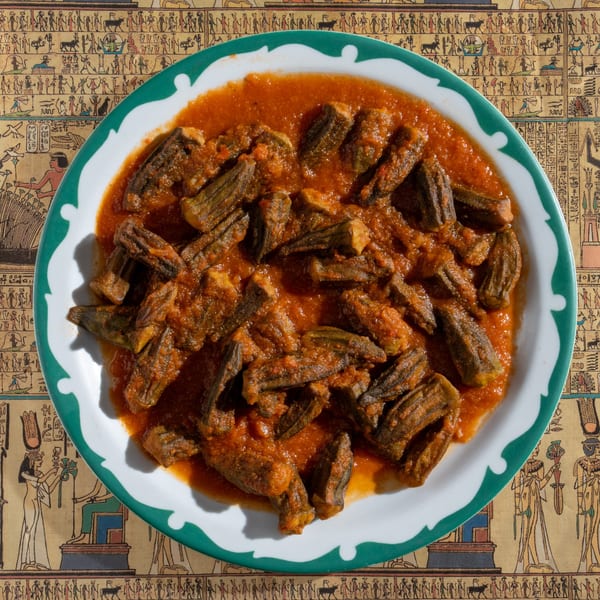 Egyptian okra stew in a white and green bowl, on a tablecloth with hieroglyphic patterns.