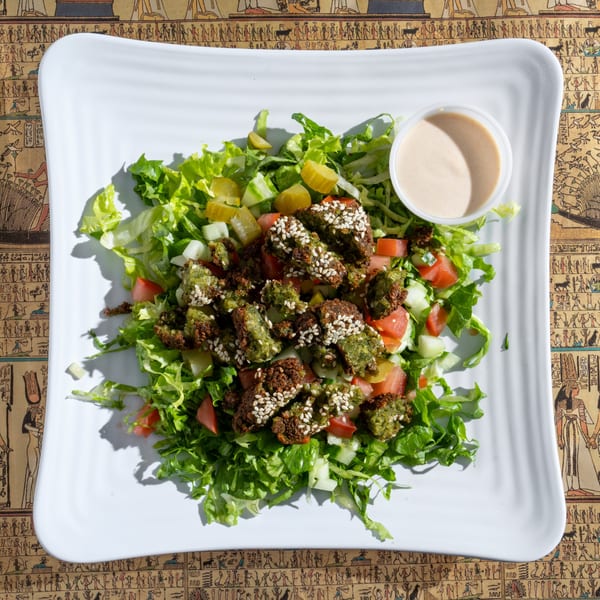 King Tut's falafel salad with lettuce, tomatoes, cucumbers, pickles, and a side of dressing.