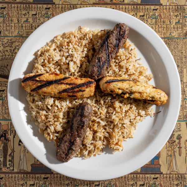 King Tut's Egyptian kofta and chicken kebab with rice on a white plate, on a hieroglyphic tablecloth.