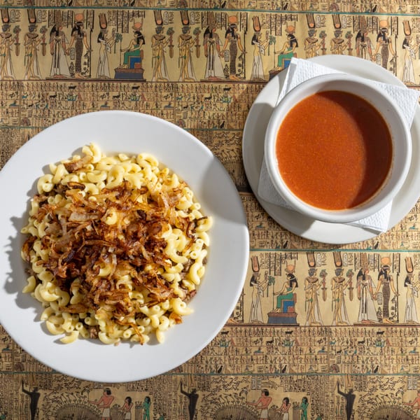 King Tut's Koshary, a pasta dish with crispy onions, and a side of tomato sauce on an Egyptian-themed tablecloth.