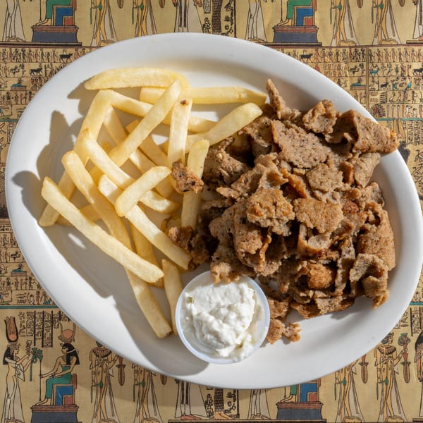 King Tut's gyro platter with sliced meat, golden fries, and a side of white sauce on an Egyptian-themed tablecloth.