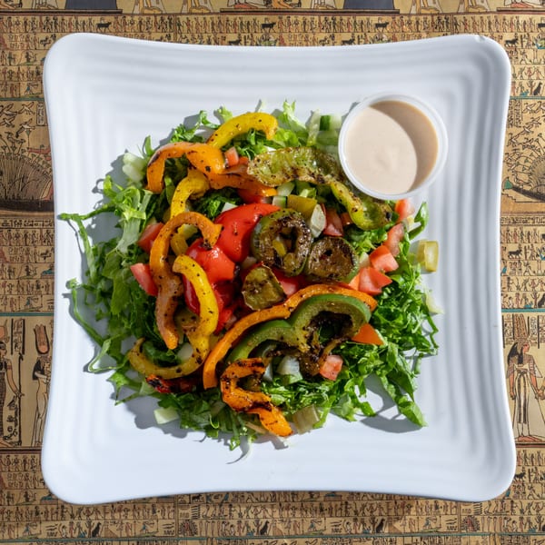 A King Tut salad with grilled bell peppers, lettuce, tomatoes, and dressing on a white plate.