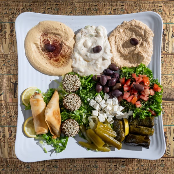 A large platter of Egyptian appetizers including hummus, baba ghanoush, falafel, stuffed grape leaves, and salad.